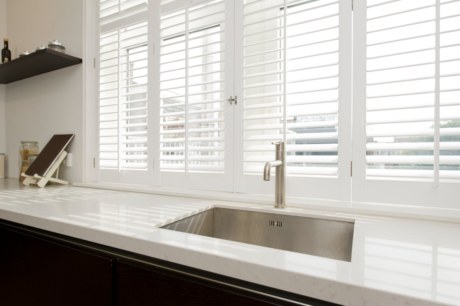 White plantation shutters above a kitchen sink with bright filtered light